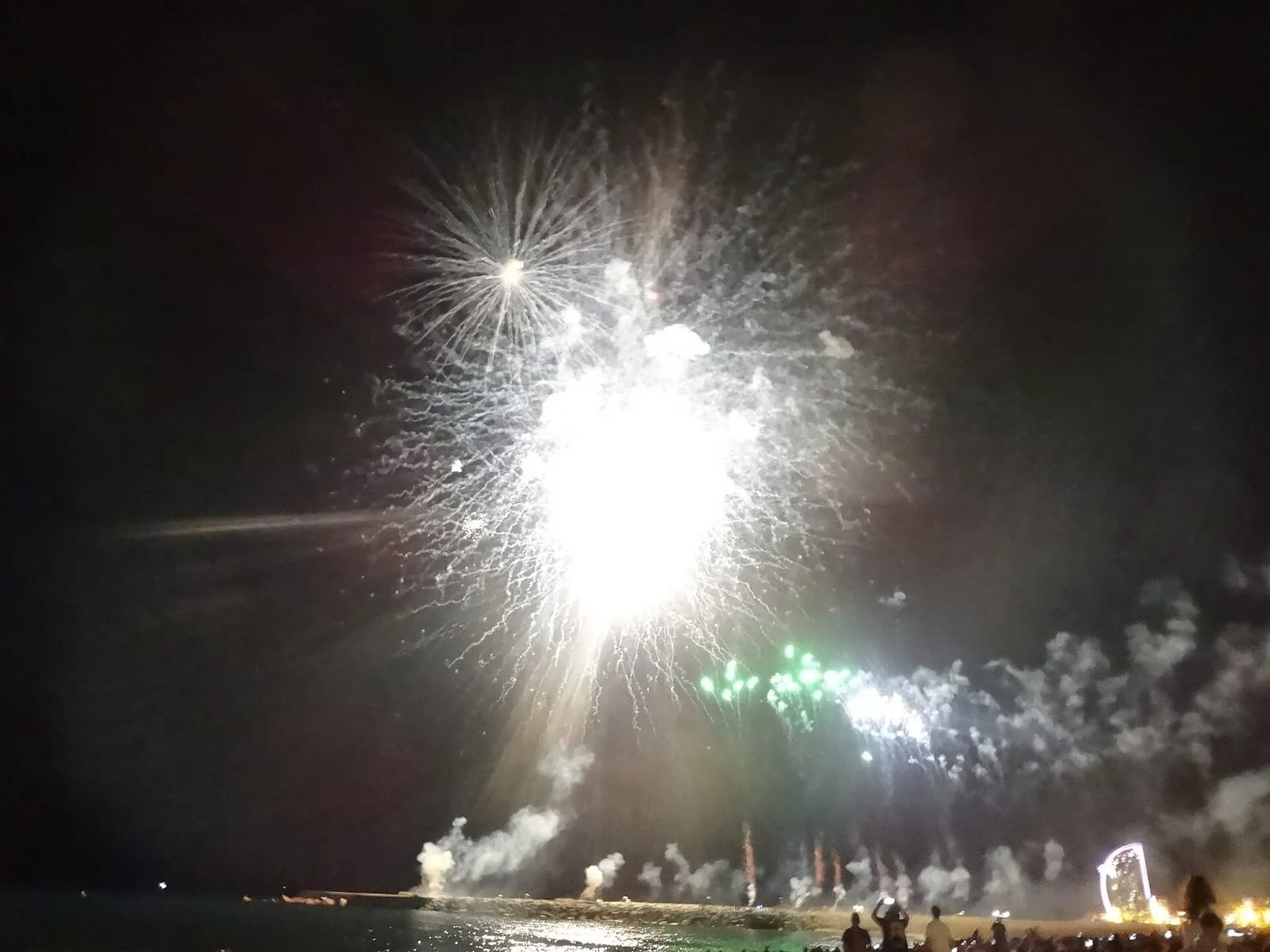 Una passerella in legno che attraversa la sabbia della Barceloneta verso il mare, con una piattaforma ombreggiata accanto