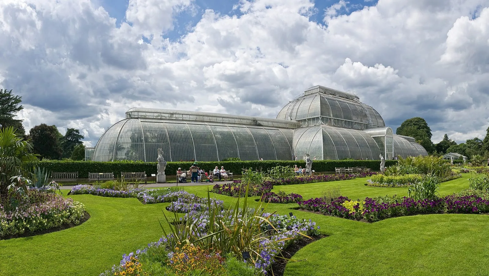 Un ampio sentiero pianeggiante attraverso i giardini botanici di Kew, con la Palm House sullo sfondo