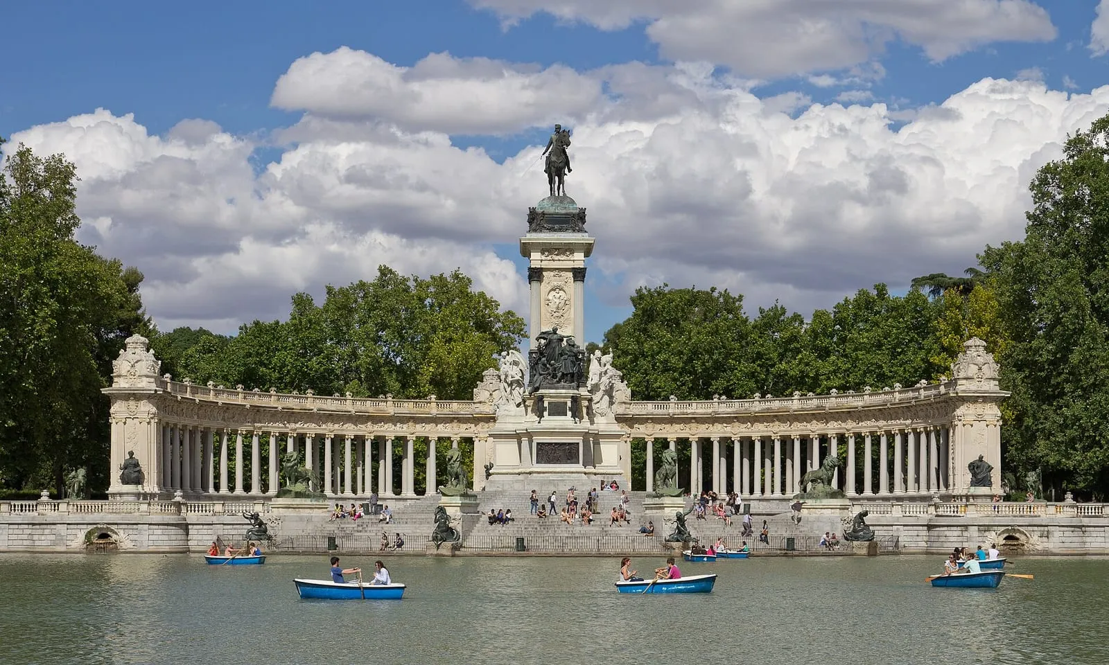 A broad paved avenue lined with clipped trees running through El Retiro towards the lake