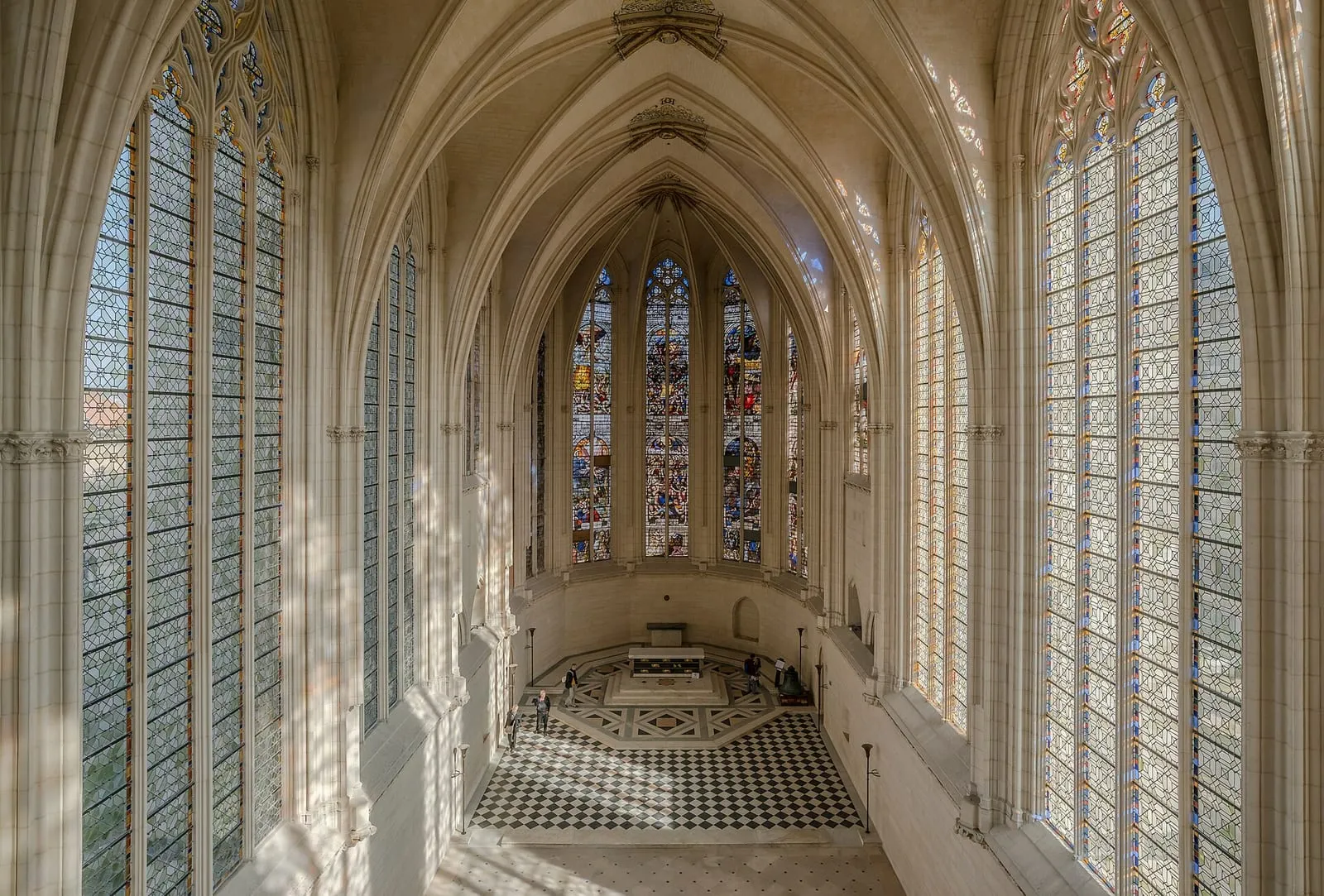 Stained glass walls of the Sainte-Chapelle upper chapel glowing above a worn stone floor