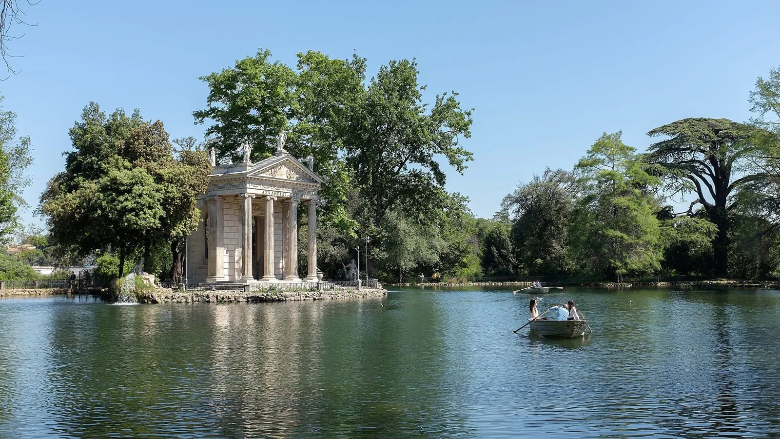 Un ampio viale asfaltato fiancheggiato da pini a Villa Borghese, che conduce verso la Galleria